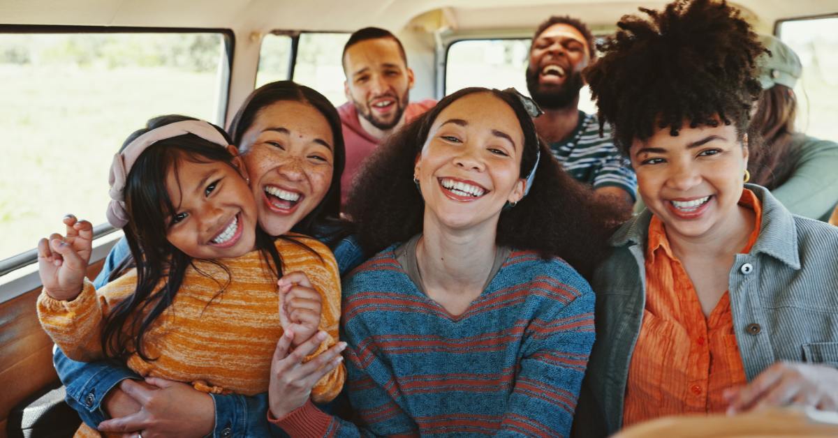 A group of six people, including a young girl and adults, laughing and smiling inside a vehicle with windows.